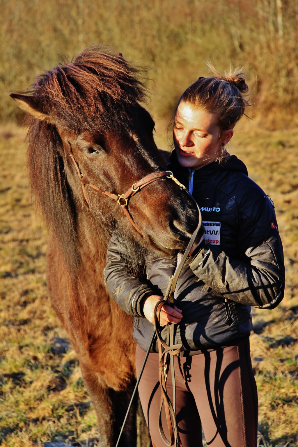 Kvinde med hest i solskin på mark.